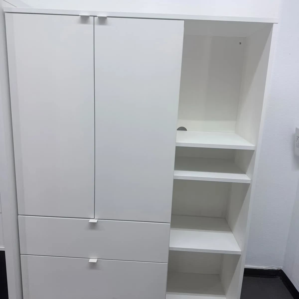 Weißer Schrank mit zwei Türen und Schubladen, daneben ein offenes Regal
